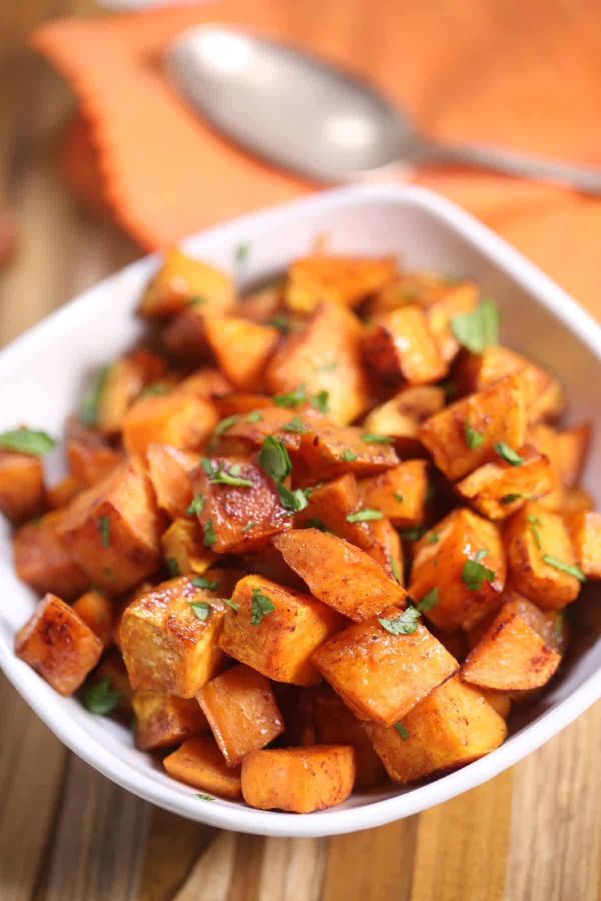 A close-up shot of perfectly roasted brown sugar sweet potato chunks, slightly caramelized and glistening, in a rustic serving bowl, garnished with a sprig of fresh rosemary. Warm, inviting lighting.