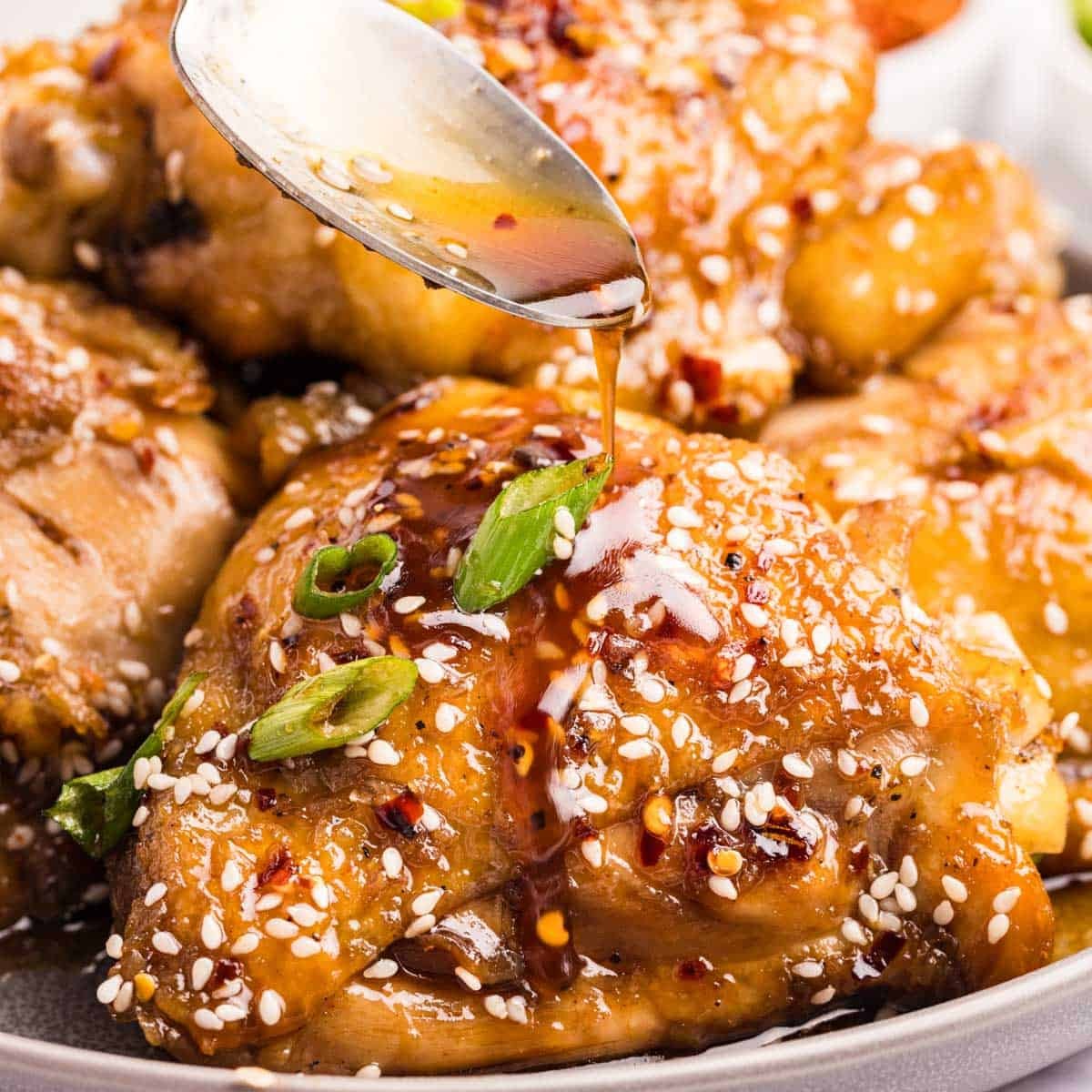 Close-up of golden sticky honey garlic chicken thighs in a slow cooker, garnished with green onions and sesame seeds