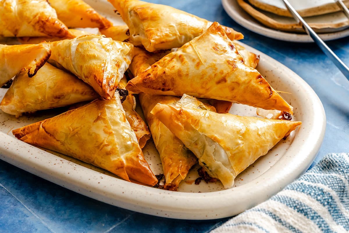 Golden brown spinach feta pastry triangles on a serving platter, close-up, with steam, rustic kitchen background