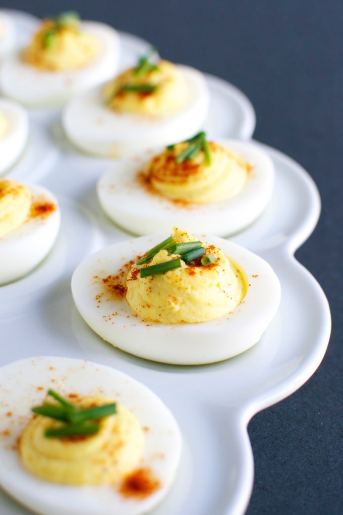 Platter of perfectly arranged creamy deviled eggs, garnished with paprika and chives
