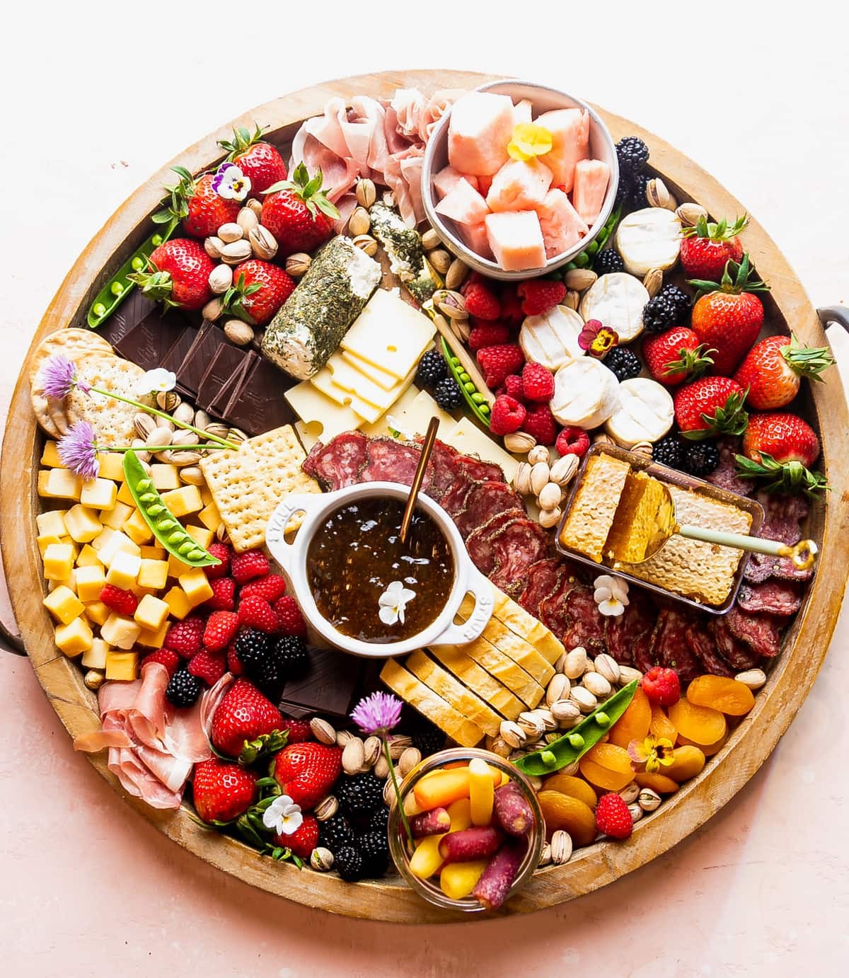overhead shot of a spring themed cheese board with various cheeses, fruits, and nuts