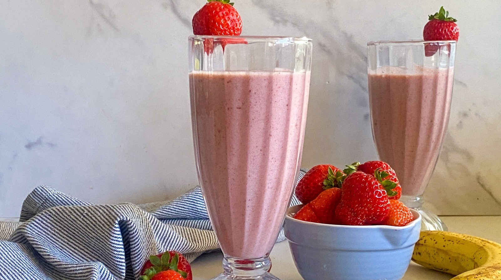 strawberry cinnamon smoothie in a glass with cinnamon sticks and fresh strawberries around it