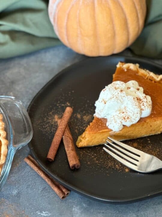 Homemade creamy pumpkin pie with flaky butter crust, garnished with whipped cream and cinnamon on a rustic wooden table