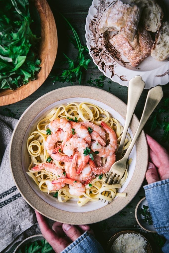 overhead shot of shrimp scampi served over pasta with a side of crusty bread