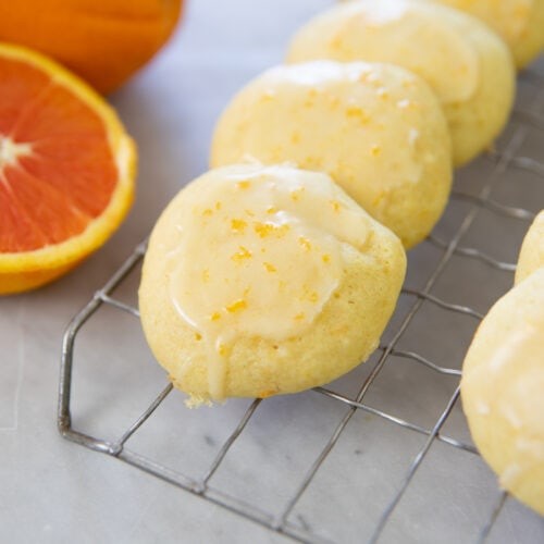 bright citrus cookies with glossy glaze on a cooling rack, vibrant colors, fresh lemons and oranges in background