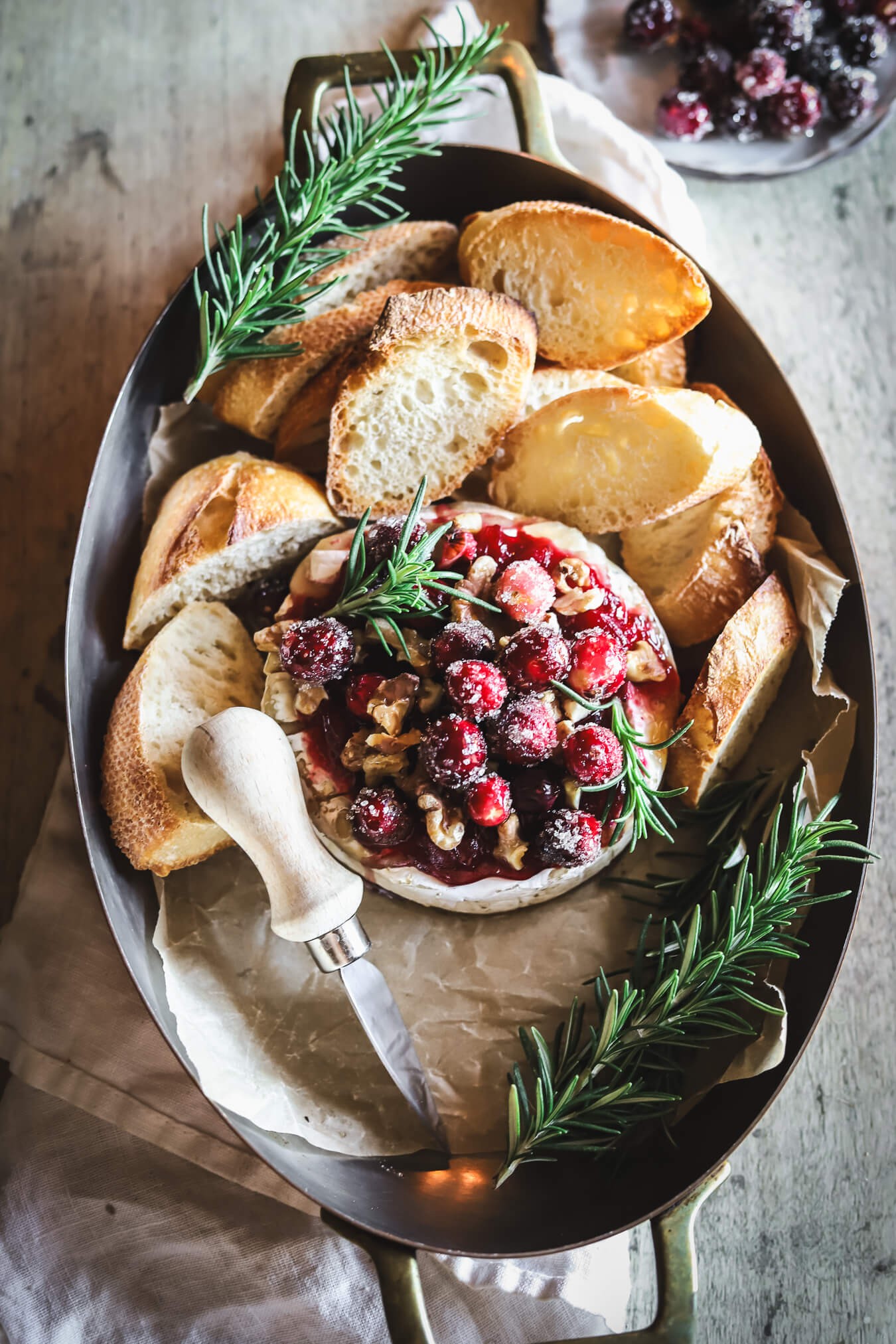 Baked Brie wheel with glistening cranberry glaze, surrounded by crackers and fresh rosemary on a rustic wooden board, ready to serve.