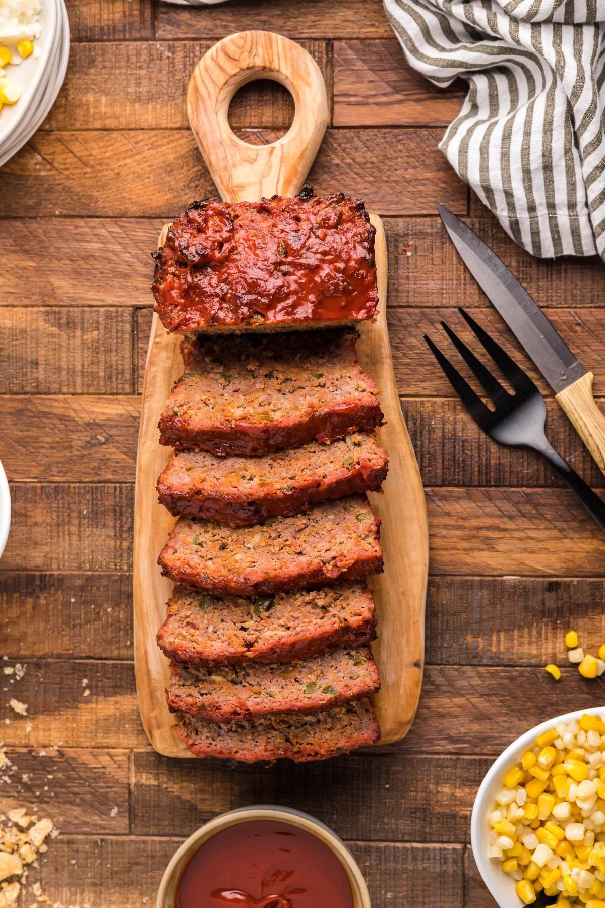 rustic meatloaf on a wooden cutting board with a knife and serving spoon beside it