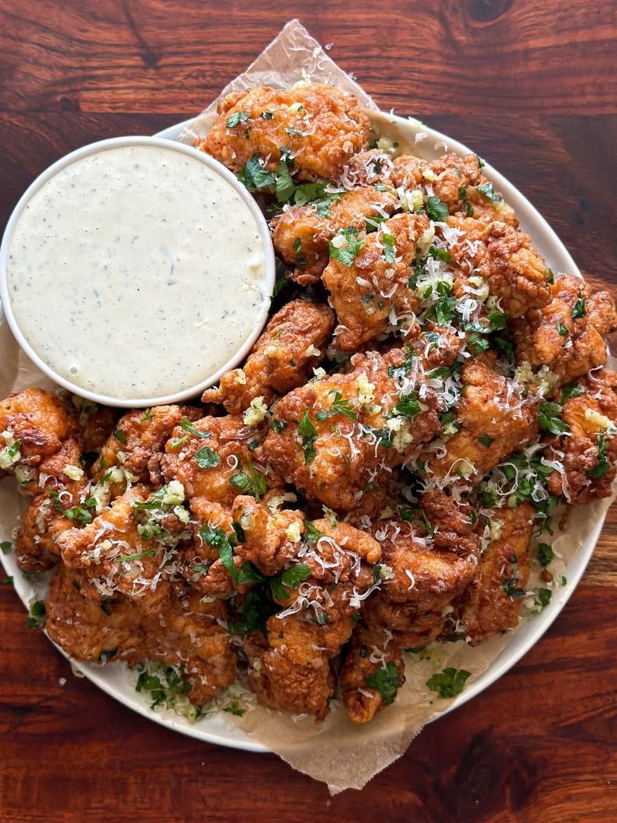 Spicy Garlic Parmesan Chicken Bites on a rustic platter with a lively party background, focus on golden brown chicken with herbs and cheese