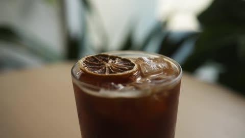 close up of a glass of cold brew iced coffee with ice cubes and a lemon slice, condensation on the glass