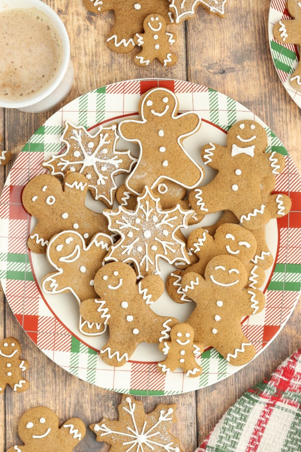 Close-up of beautifully decorated gingerbread cookies on a rustic wooden board, some with intricate white royal icing details, surrounded by festive holiday decor like cinnamon sticks and star anise