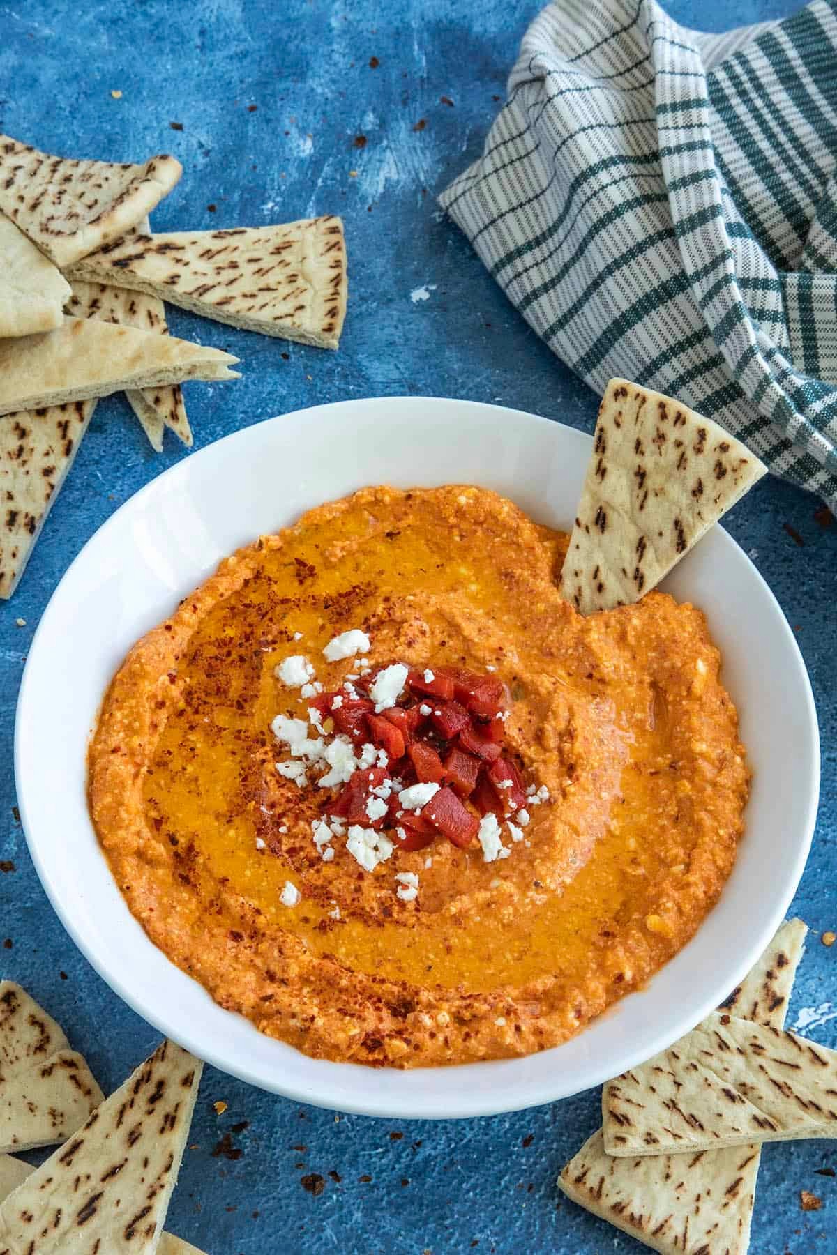 Vibrant whipped feta dip with toasted pita bread on a rustic wooden board, olives and red peppers scattered