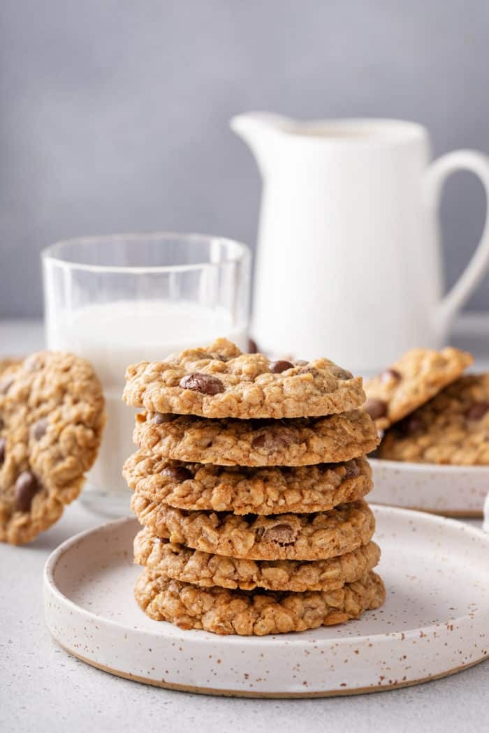 Warm, perfectly chewy oatmeal raisin cookies stacked on a cooling rack with a glass of milk, cozy kitchen background